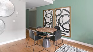 A modern dining area with a round wooden table and black chairs, a large abstract painting on the wall, and a patterned rug on the floor. - Two Bedroom Green Point Rooftop Pool BBQ (Cape Town)