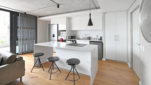 A modern kitchen with a central island, bar stools, and a pendant light. - Two Bedroom Green Point Rooftop Pool BBQ (Cape Town)