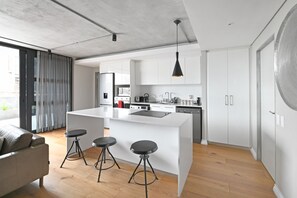 Et moderne køkken med en central ø, barstole og en hængende lampe.