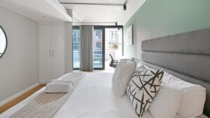 A modern bedroom with a large bed, white curtains, and a view of the outside. - Two Bedroom Green Point Rooftop Pool BBQ (Cape Town)