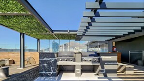 An outdoor rooftop bar with a grill and seating area, surrounded by a wooden deck and a green wall. - Two Bedroom Green Point Rooftop Pool BBQ (Cape Town)