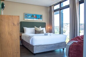 Quarto de hotel com uma cama grande, um guarda-roupa de madeira, um quadro na parede e vista para a cidade pela janela.