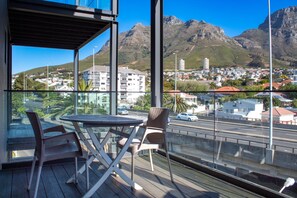 Un balcon avec une table et des chaises, d’où l’on peut admirer la vue sur la ville et les montagnes.