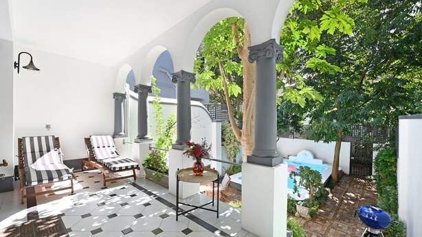 A sunlit patio with lounge chairs, a small table with a vase, and a pool in the background. - Elegant Three Bedroom Home (Cape Town)