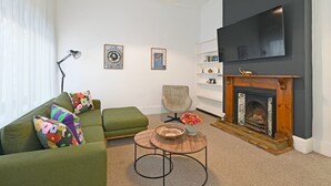 A modern living room with a green sofa, a round coffee table, a fireplace, and a flat-screen TV mounted on the wall. - Elegant Three Bedroom Home (Cape Town)