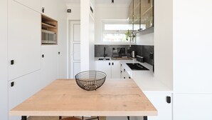 A modern kitchen with white cabinetry, a wooden table, and a black wire basket. - Green Point Micro Lock Up and Go (Cape Town)