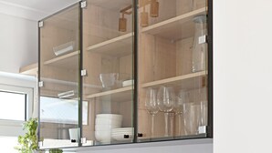 A kitchen with wooden cabinets, a glass-fronted cabinet, and a potted plant. - Green Point Micro Lock Up and Go (Cape Town)