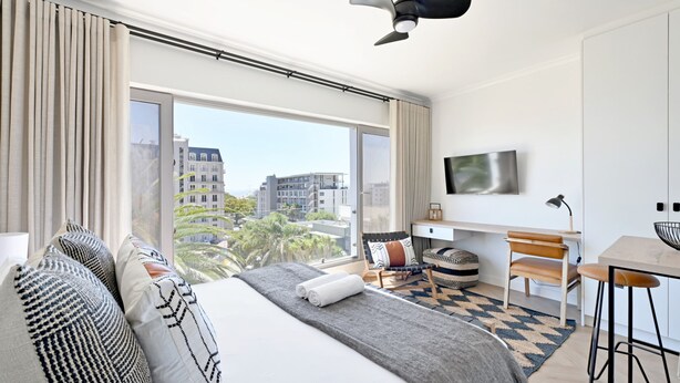 A modern hotel room with a large bed, a desk, a chair, and a TV. - Green Point Micro Lock Up and Go (Cape Town)