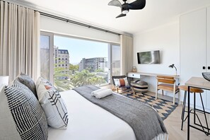A modern hotel room with a large bed, a desk, a chair, and a TV. - Green Point Micro Lock Up and Go (Cape Town)