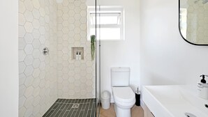 A bathroom with a hexagonal tile wall, a shower, a toilet, and a white sink with a mirror. - Green Point Micro Lock Up and Go (Cape Town)