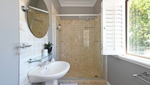 A bathroom with a white sink, a glass shelf, a mirror, and a shower with beige tiles. - Two Bed Table Mountain Spacious (Cape Town)