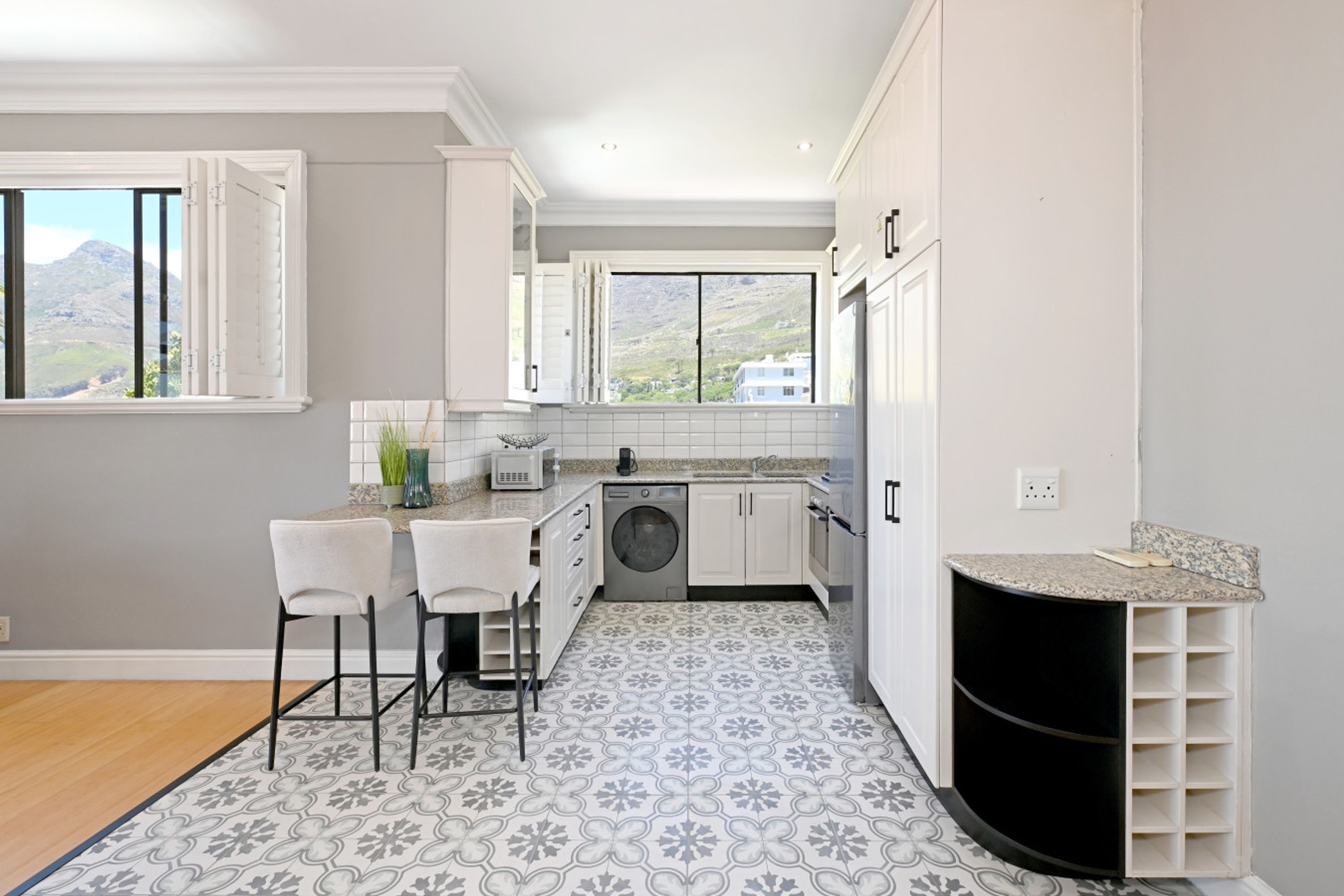A modern kitchen with white cabinets, a built-in washing machine, and a large window offering a mountain view.