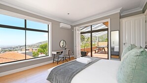 Une chambre avec un grand lit, un bureau et une vue sur la ville grâce à de grandes fenêtres.