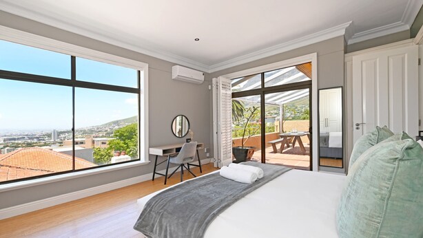 A bedroom with a large bed, a desk, and a view of the city through large windows. - Two Bed Table Mountain Spacious (Cape Town)