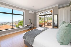 A bedroom with a large bed, a desk, and a view of the city through large windows. - Two Bed Table Mountain Spacious (Cape Town)