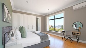 A bedroom with a large bed, a desk, a chair, and a view of the city through a large window. - Two Bed Table Mountain Spacious (Cape Town)
