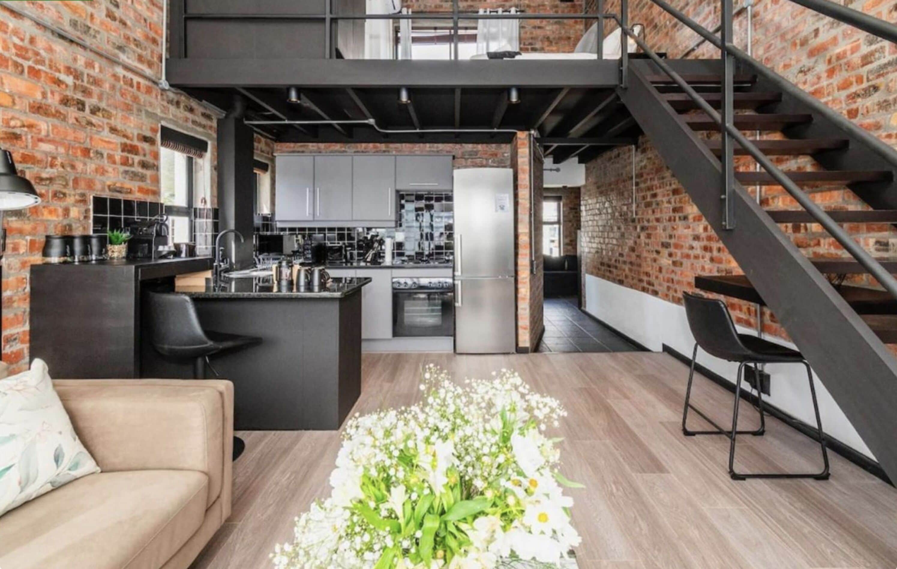 Una cucina moderna con isola centrale, una scala e un angolo soggiorno con divano e fiori.