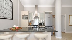 Una cocina moderna con una isla central, taburetes de bar, una campana extractora de acero inoxidable y un cartel grande en la pared.