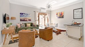 Una sala de estar moderna con un sofá verde, dos sillas de madera, una mesa de centro y una zona de comedor con una mesa y sillas blancas.