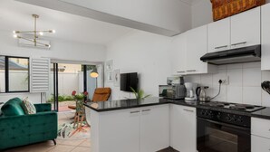 Una cocina moderna con armarios blancos, una estufa negra y un comedor con un sofá verde.