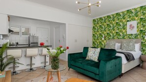 Una sala de estar moderna con un sofá verde, una mesa de centro y una zona de comedor con taburetes de bar.