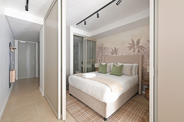 A modern bedroom with a large bed, a sliding door, and a bathroom visible through a glass partition. - Quiet 1bed Green Point Retreat Central and Elegant (Cape Town)