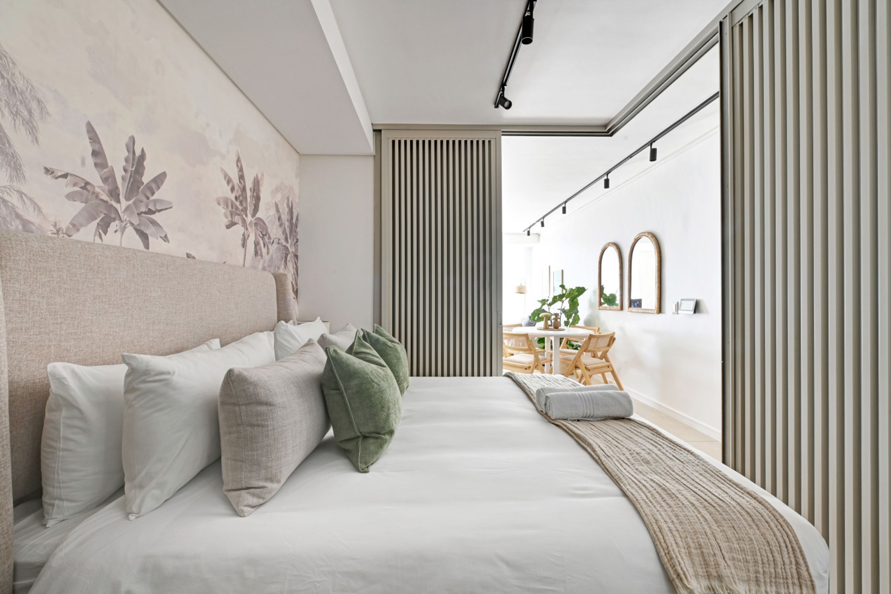 Un dormitorio moderno con una cama grande, un cabecero, una mesita de noche y vistas a un comedor a través de una puerta corrediza.