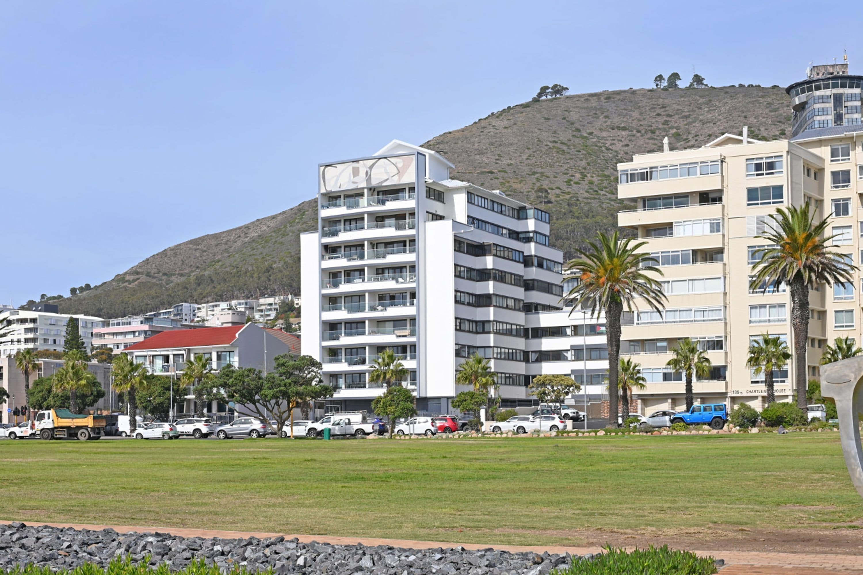Un hotel de varios pisos con techo plano, rodeado de césped y palmeras.