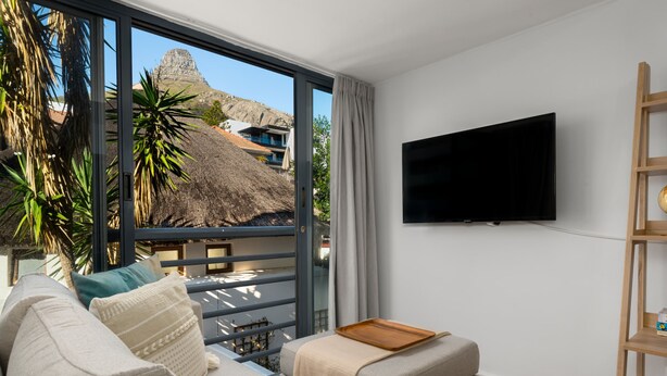 Een moderne woonkamer met een bank, een flatscreen televisie en een balkon met uitzicht op een berg en gebouwen.