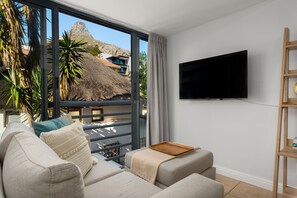 Una sala de estar moderna con un sofá, un televisor de pantalla plana y un balcón con vistas a una montaña y edificios.