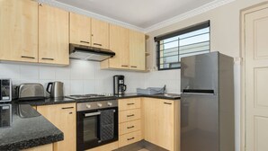 A kitchen with wooden cabinets, a stainless steel refrigerator, a stove, and a coffee maker. - Planet Africa Studio Pool Gym (Cape Town)