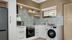 A compact kitchen with white cabinets, a microwave, an oven, and a washing machine. - Sea Point Oasis Private Garden Pool Gym and BBQ (Cape Town)