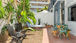 A patio area with a table and chairs, a small garden with plants, and a view of a building in the background. - Sea Point Oasis Private Garden Pool Gym and BBQ (Cape Town)