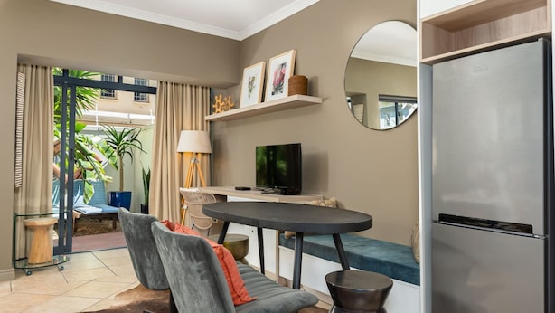 A modern living room with a sofa, chairs, a dining table, a TV, and a refrigerator. - Sea Point Oasis Private Garden Pool Gym and BBQ (Cape Town)