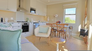 Une cuisine moderne avec des meubles blancs, un four encastré et un coin repas comprenant des chaises et une table en bois.