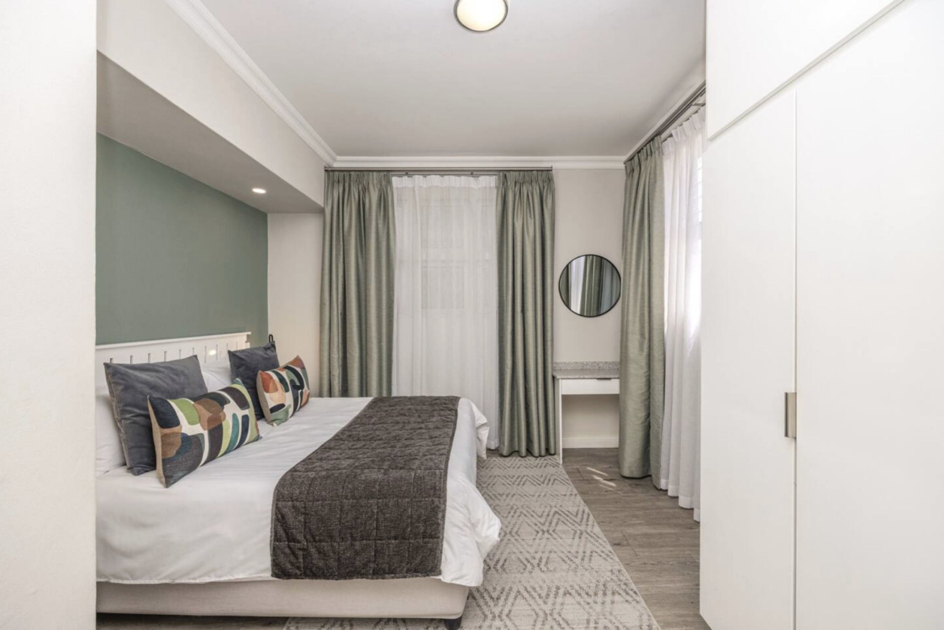 A bedroom with a bed, a bedside table, a mirror, and a wardrobe.
