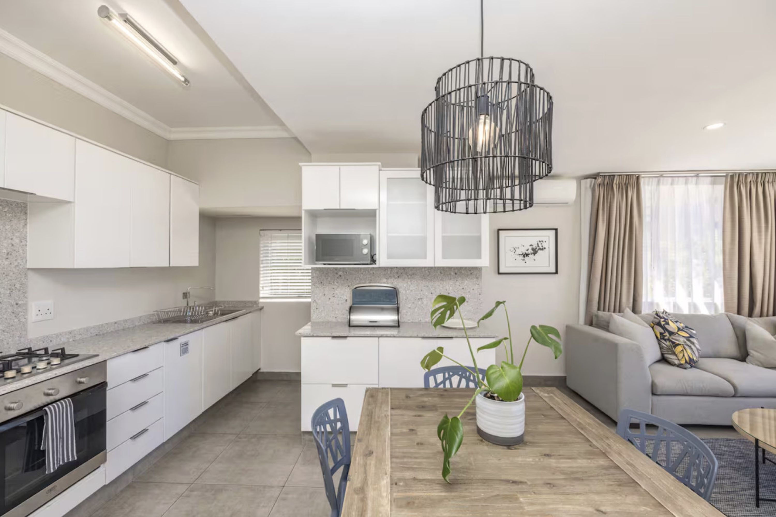 Une cuisine moderne avec des meubles blancs, un four à micro-ondes encastré et une table à manger en bois avec des chaises.