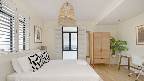 Un dormitorio con cama, armario, escritorio y ventana con persianas.
