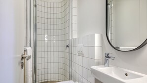 Et badeværelse med brusebad, toilet, håndvask og spejl.