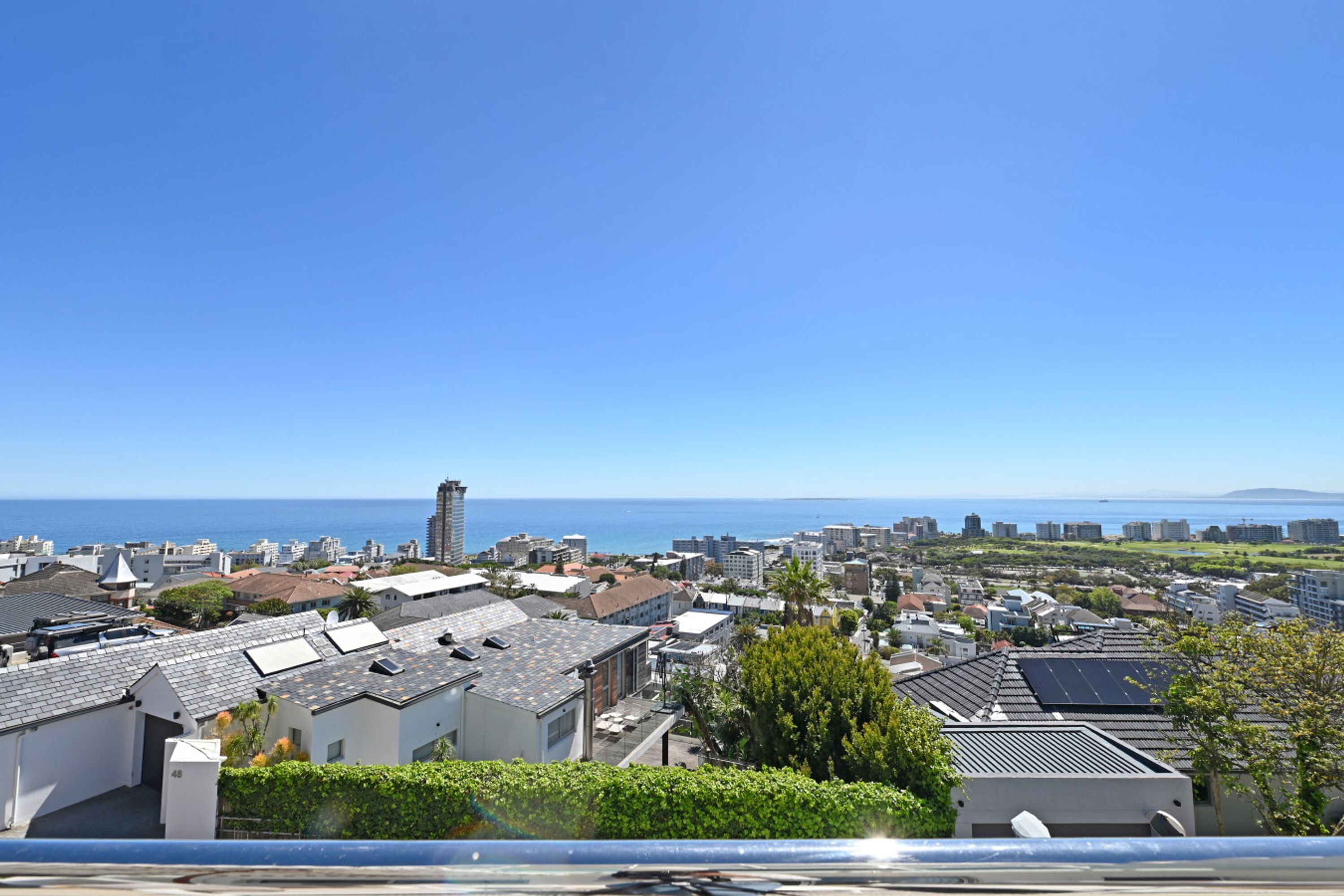 A coastal residential area with buildings, a clear blue sky, and the sea in the background.
