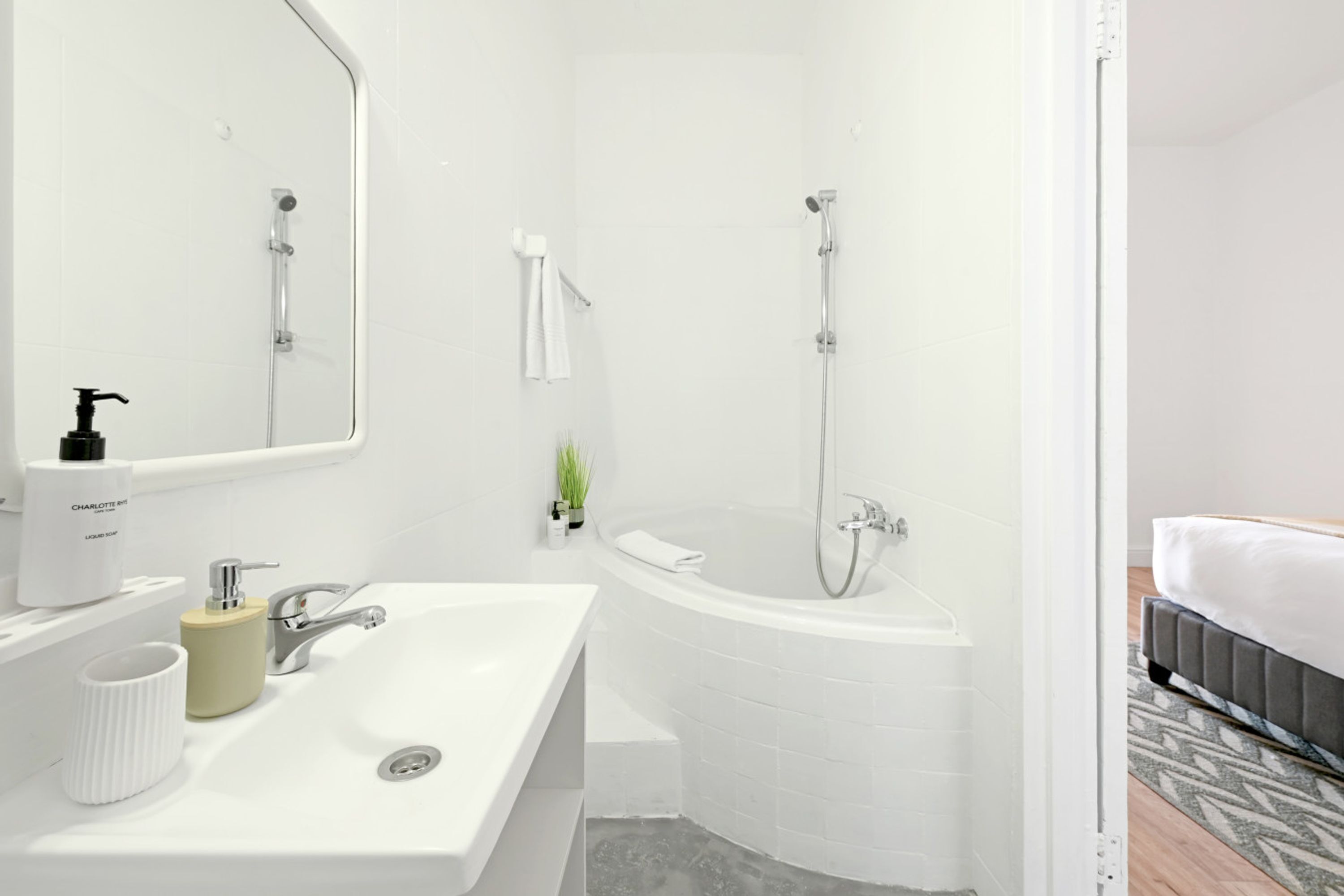 A modern bathroom with a white sink, a bathtub, and a shower. There is a mirror above the sink and a towel hanging on the wall.