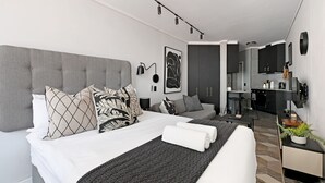 Una habitación de hotel moderna con una cama grande, un escritorio, una silla y una kitchenette.