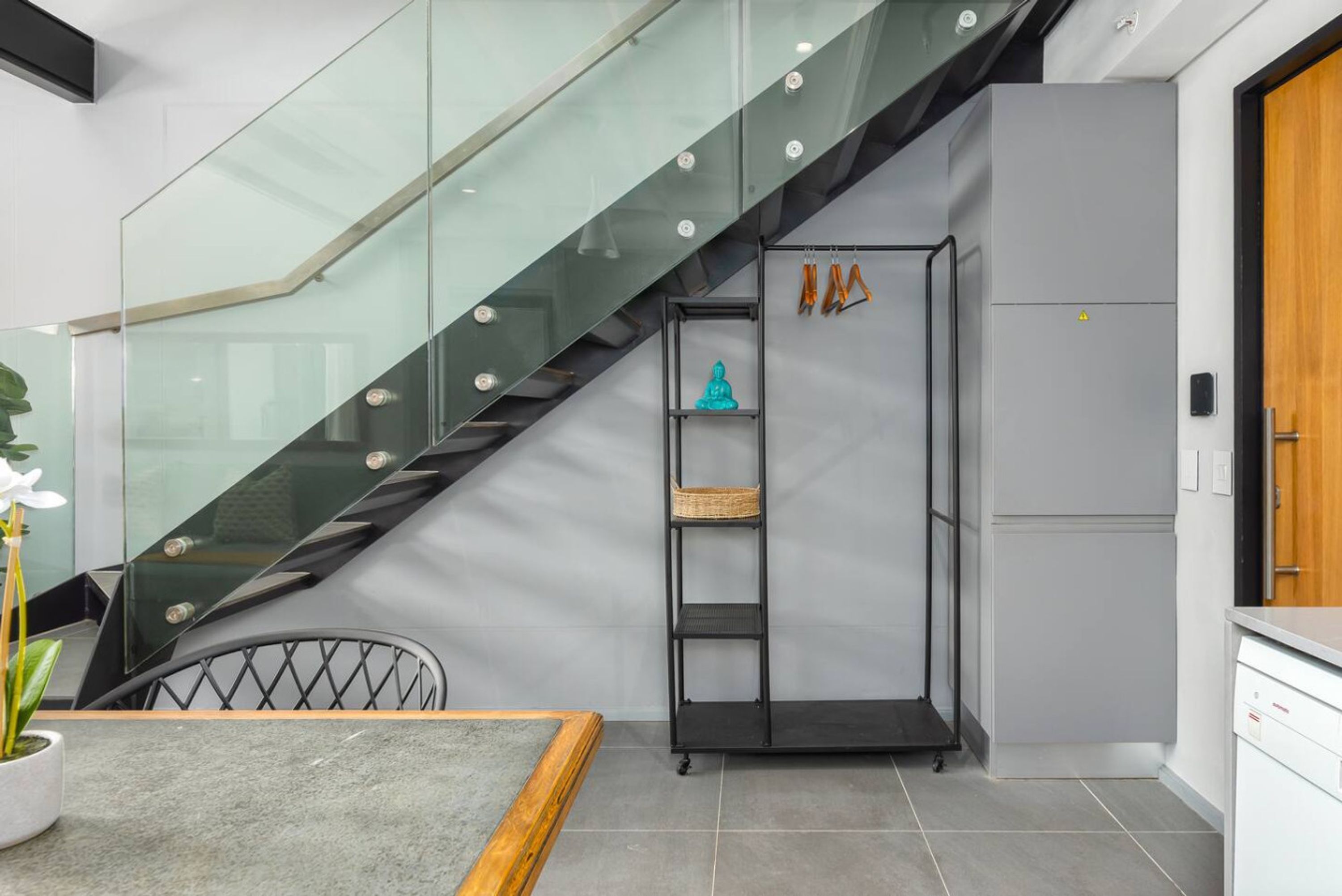 A modern kitchen with a grey refrigerator, a built-in oven, and a glass staircase.