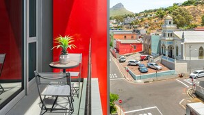 Un balcon avec un mur rouge, une plante en pot et une table avec des chaises.