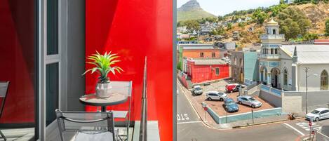 A balcony with a red wall, a potted plant, and a table with chairs.
