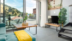 Un salon moderne doté d’une grande fenêtre, d’un téléviseur à écran plat et d’un coin repas avec une table et des chaises.