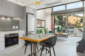 A modern kitchen with a dining area, large windows, and a view of a hillside. - Stylish 1bed Secure Mountain Views (Cape Town)