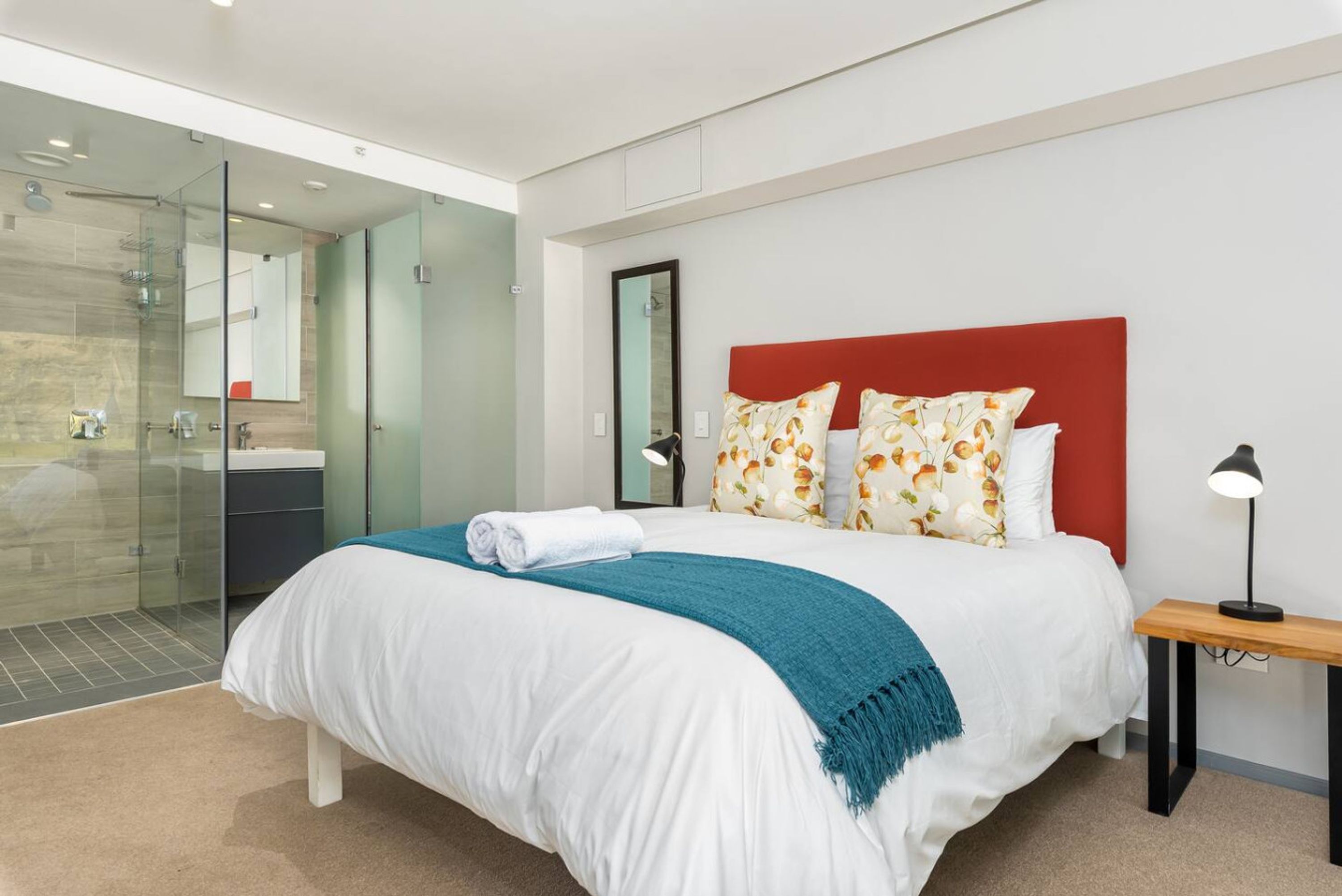 Une chambre d’hôtel moderne avec un grand lit, une douche en verre et une table de chevet en bois.