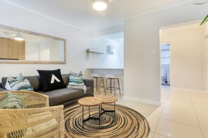 A modern living room with a grey sofa, wicker chairs, a coffee table, and a large mirror. - Chic Sea Point Retreat Walk to the Promenade Caf s (Cape Town)
