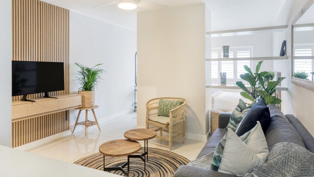 Un salon moderne doté d’un téléviseur à écran plat, de lambris en bois, d’un fauteuil en osier, d’un canapé gris et d’un ventilateur de plafond.